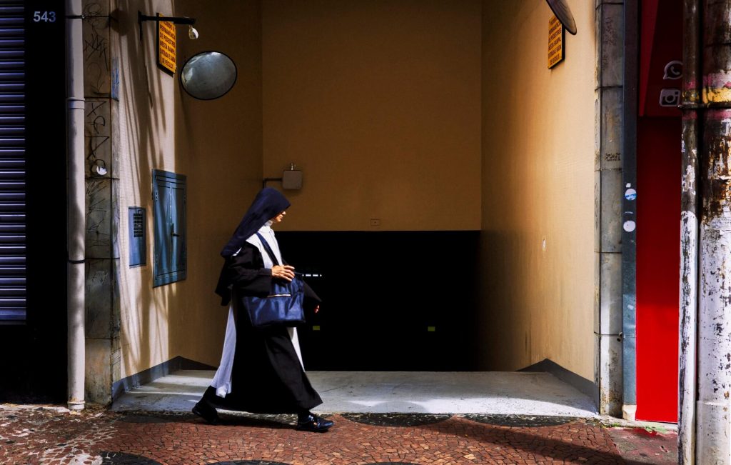Pessoa com hábito religioso caminhando em calçada, fotografia de Alexandre de Olanda
