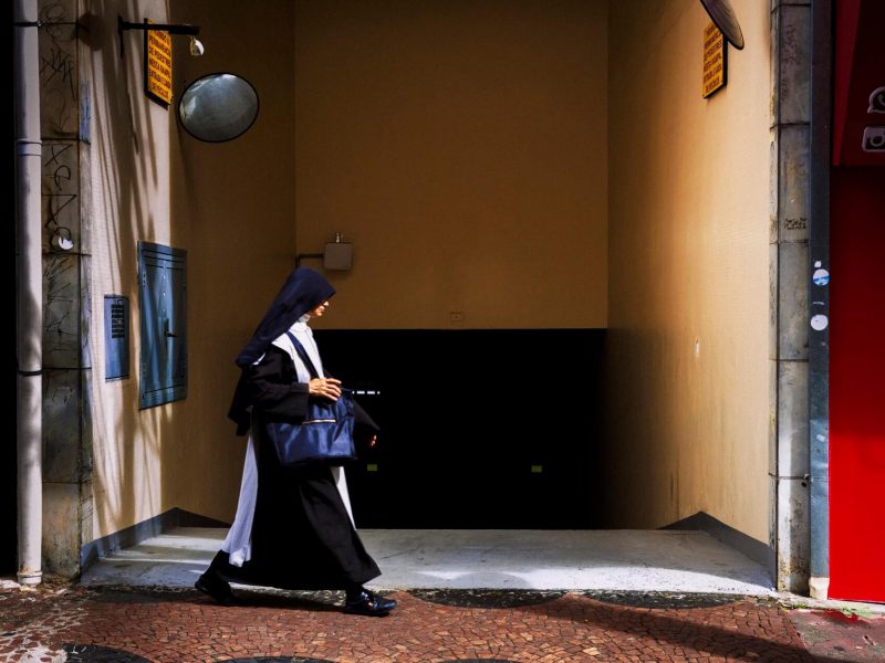 Pessoa com hábito religioso caminhando em calçada, fotografia de Alexandre de Olanda