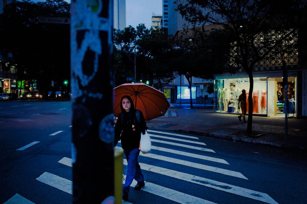 Pessoa atravessando rua com guarda-chuva laranja, fotografia de Alexandre de Olanda
